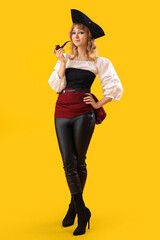 Young woman dressed for Halloween as pirate with smoking pipe on yellow background