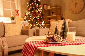 Christmas cookies with glass of milk and decor on table in living room at night