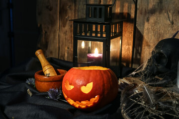 Halloween composition with jack-o-lantern, mortar, pestle and skull on wooden table