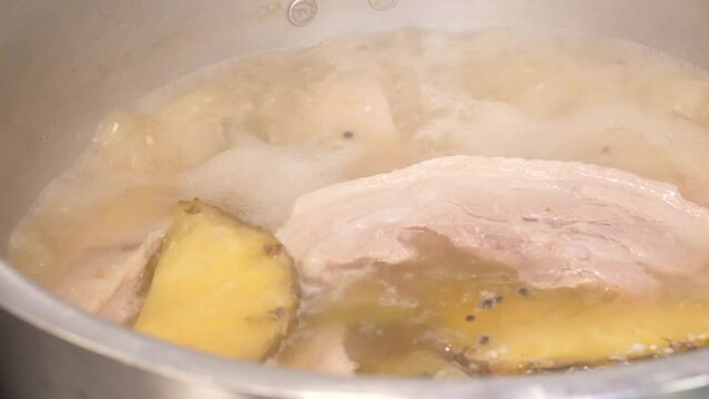 커다란 들통 가득 담긴 채수에 통삼겹살을 넣고 부드럽게 삶은 수육을 칼로 써는 모습
 