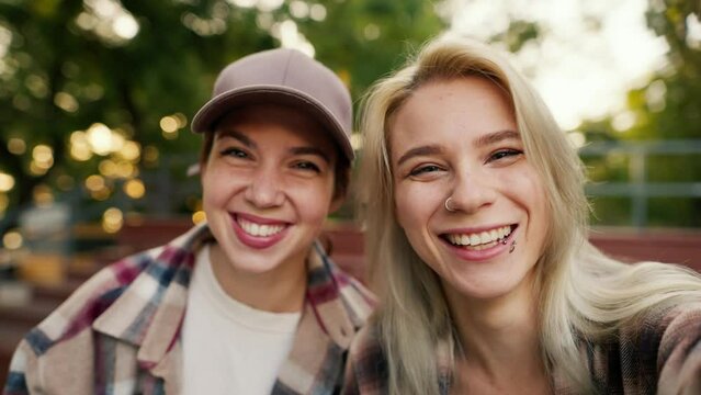 Selfie of happy two girls friends in plaid shirts sticking out their tongues and smiling near a skatepark on a sunny summer day