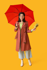 Beautiful young woman with autumn leaves and umbrella on yellow background