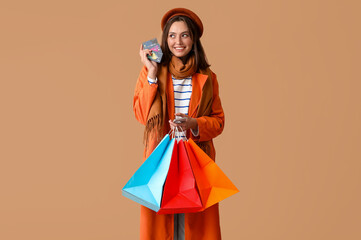 Young woman with shopping bags, credit cards and mobile phone on brown background