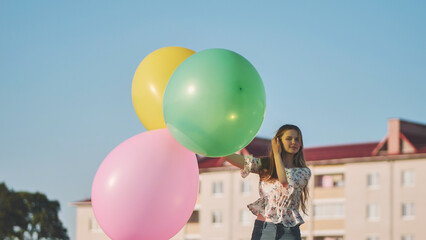 A girl happily poses with large with colorful balloons in the city.