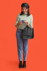 Young woman with shopping bags, mobile phone and credit cards on red background