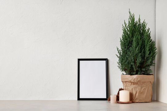 Minimal Nordic white winter home interior design template. Blank picture frame, juniper in pot, candles on beige table and empty white wall background
