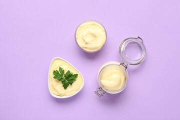 Obraz na płótnie Canvas Bowls and jar of fresh mayonnaise on lilac background