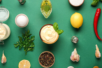 Fototapeta na wymiar Bowl of fresh mayonnaise and ingredients on green background