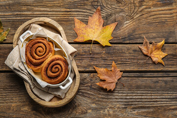 Baking dish of tasty cinnamon rolls and autumn leaves on wooden background