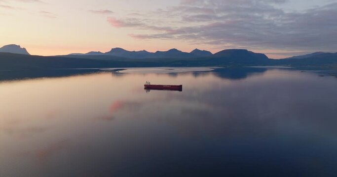 High angle aerial view of red cargo ship anchored in ocean, perfect vivid sunset