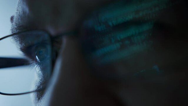 Close up shot of portrait of software engineer coding on computer. Line of hack code run in reflection on eyeglasses 