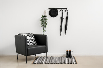 Stylish armchair, shoes and umbrellas hanging on light wall