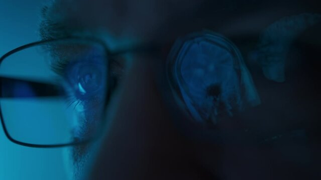 Male doctor eyes in eyeglasses late at night looking in front of MRI data on laptop. Macro shot footage