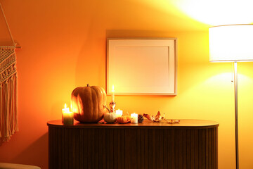 Wooden cabinet with pumpkins, burning candles and autumn leaves in dark living room