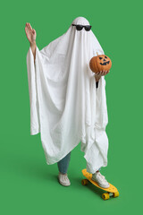 Woman in Halloween costume of ghost with pumpkin and skateboard on green background