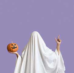 Woman in Halloween costume of ghost with pumpkin pointing at something on lilac background