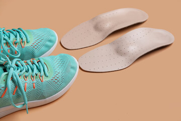 Pair of sneakers and orthopedic insoles on color background, closeup