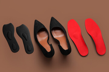Pair of stylish high heeled shoes and orthopedic insoles on color background