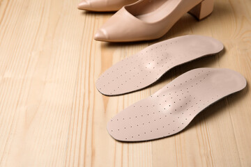 Pair of orthopedic insoles and stylish high heeled shoes on wooden background