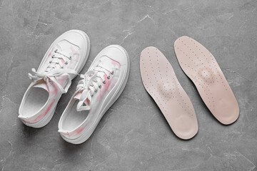 Pair of orthopedic insoles and stylish sneakers on grunge background