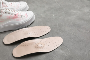 Pair of orthopedic insoles and stylish sneakers on grunge background