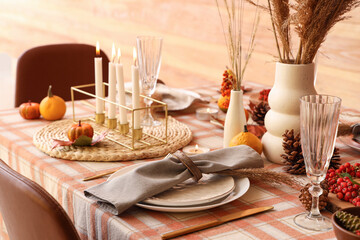 Autumn table setting with pumpkins, pine cones and burning candles, closeup