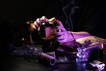 Witch with crystal ball at dark table, closeup