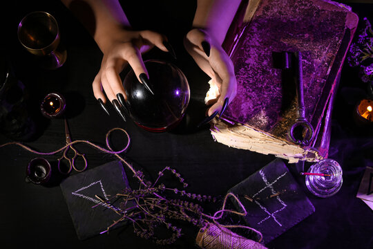 Witch with crystal ball at dark table, closeup