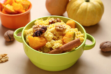 Pot of tasty millet porridge with pumpkin on orange background