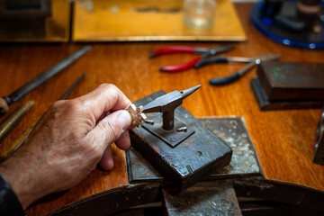 Goldsmith creating and repairing in his crafting gold jewelry workshop with an anvil. Jeweler working in a silver jewel.