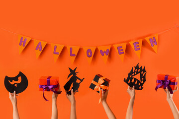 Women with Halloween gifts and paper decor on orange background