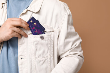 Young man putting credit cards into pocket on brown background, closeup