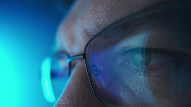 Close up shot of software engineer coding on computer on day time. Line of hack code run in reflection on eyeglasses 