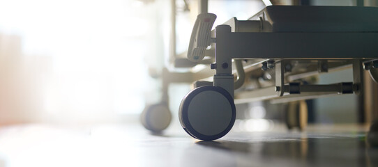 Closeup, hospital and bed with a clean floor, empty room and lens flare with a wheel, ergonomics design and healthcare. Zoom, sunshine light and clinic space with comfort, metal and medical furniture