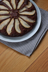 Homemade Chocolate round cake with sliced pears on the top on a white plate on wooden table