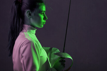 Young woman fencer profile portrait with fencing equipment holding sword in her hand - obrazy, fototapety, plakaty