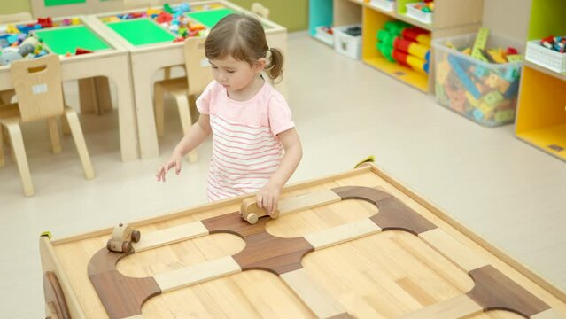 Girl toddler plays with wooden toy cars pushing them along the road on wood table in Playroom - slow motion