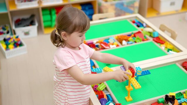 Creative Child Girl Building Tower With Constructor Bricks on Big Table in Playroom - Slow motion. Creativity Development and Yearly Educational Games for Children
