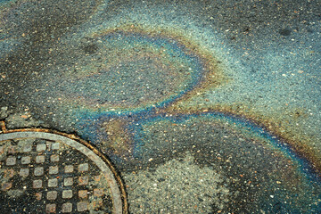 Rainbow stains of gasoline against the background of asphalt and a manhole