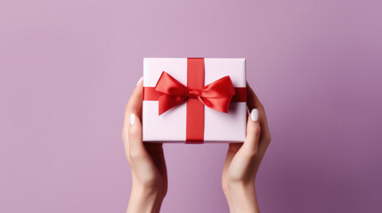 A woman's hands hold a white gift box with a red bow and ribbons on pink background