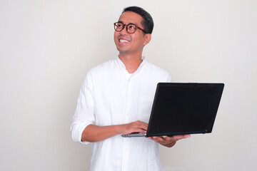 A man smiling and looking to upper right corner while holding a laptop