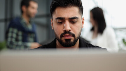 Seriously focused determined young bearded businessman or freelancer sitting at the table,