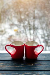 Obraz na płótnie Canvas two heart shaped mugs with tea on the background of a window in winter 