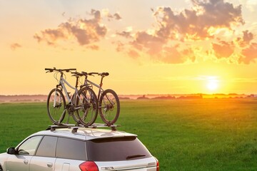 Mounted sport mountain bicycle silhouette on the car roof with evening sunlight rays background. Concept of safe items transportation using a car with roof rack