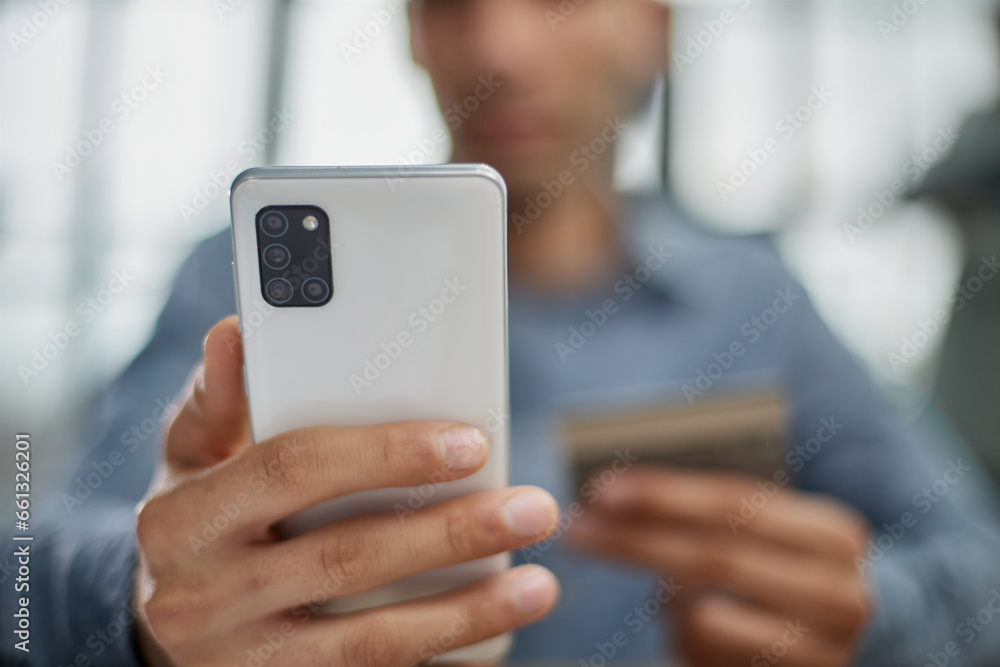 Wall mural man selects a credit card from several and enters it number into a smartphone to pay online. online 