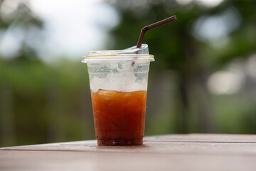 Iced americano coffee in plastic cup on wood table with nature background