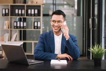 Young handsome man typing on tablet and laptop while sitting at the working wooden table modern office.