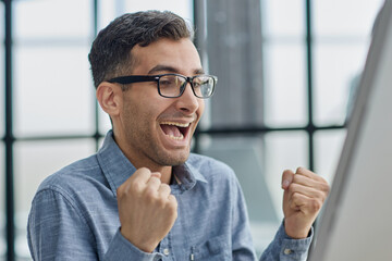 Excited modern businessman sitting at office desk and rejoicing his success