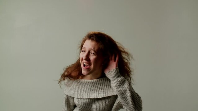 A young lady demonstrates misunderstanding her interlocutor due to poor hearing. A girl cannot hear the speaker because of loud music or noise in the room and asks to repeat. Looks at camera.
