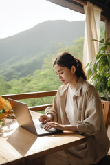 Fototapeta premium Digital nomad woman working at a table with a computer in the background views of a mountain and a valley. Work online in travel concept